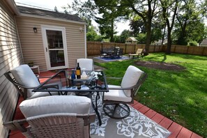 Une terrasse avec une table en verre et quatre chaises, un petit jardin et une clôture en bois.