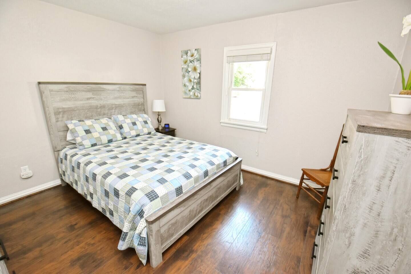 Een slaapkamer met een bed, nachtkastje, lamp, raam en een kaptafel.