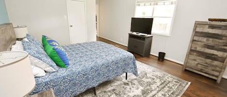 Une chambre à coucher avec un lit, une télévision, une commode et une fenêtre.