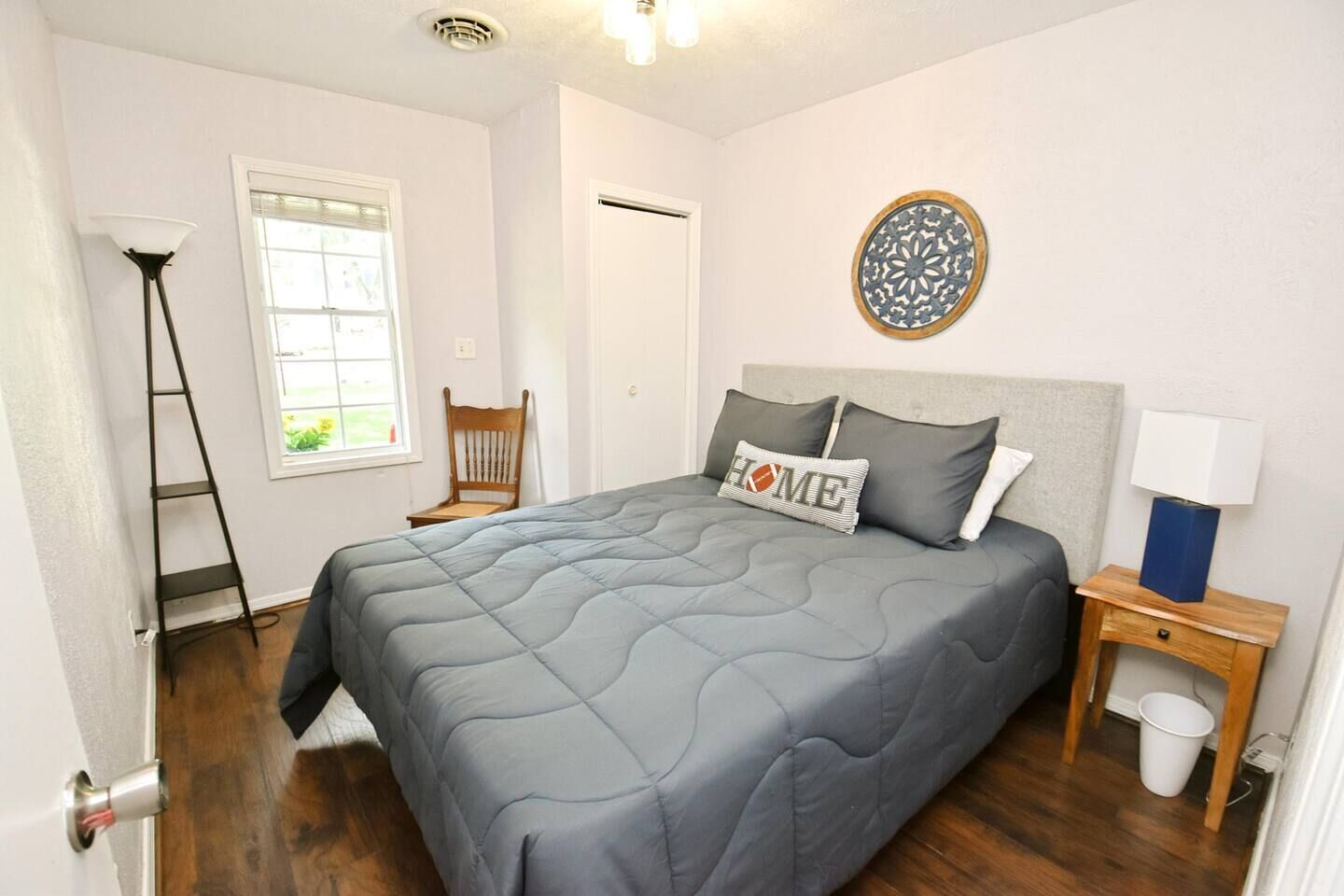 Een slaapkamer met een bed, nachtkastje, lamp, stoel en raam.