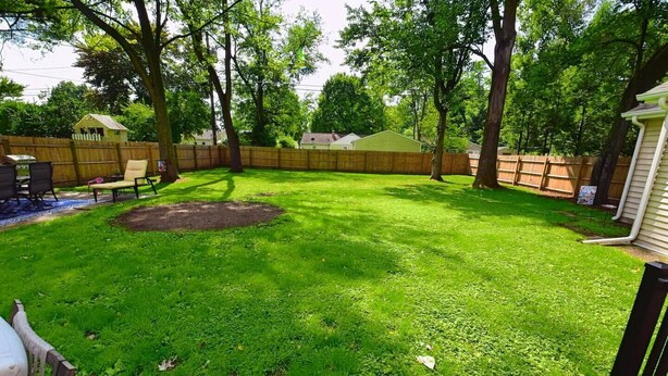 Un jardin avec une pelouse, une clôture en bois et un petit abri de jardin.