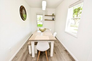 Un coin repas comprenant une table, des chaises, un bol et une fenêtre donnant sur un paysage verdoyant.
