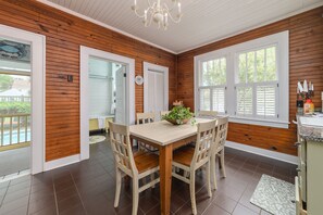 A dining area with a wooden table and chairs, a chandelier, and a view of the outdoors. - Ms. Opal's Cottage - POOL! Pet-Friendly! Ground Level (Tybee Island)