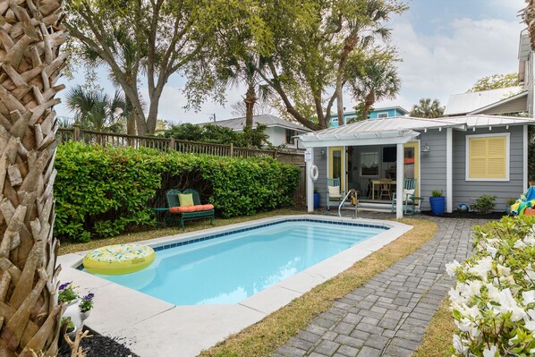 A backyard with a swimming pool, a covered patio, and a wooden fence. - Ms. Opal's Cottage - POOL! Pet-Friendly! Ground Level (Tybee Island)