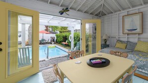 A room with a pool, a dining table, and a bed with patterned bedding. - Ms. Opal's Cottage - POOL! Pet-Friendly! Ground Level (Tybee Island)