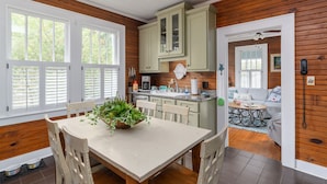A kitchen with wooden cabinets, a dining table with chairs, a coffee maker, and a window with blinds. - Ms. Opal's Cottage - POOL! Pet-Friendly! Ground Level (Tybee Island)