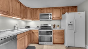 A kitchen with wooden cabinets, a microwave, an oven, a refrigerator, and a granite countertop. - 4 story condo - 100 yard walk to slopes on Sugar Mountain (Sugar Mountain)