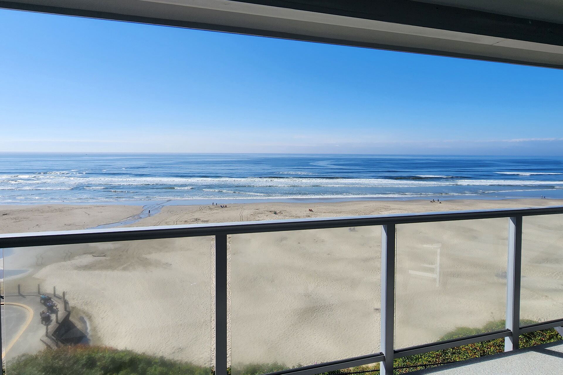 A view of a beach from a balcony with a railing, sandy beach, ocean, and clear sky.