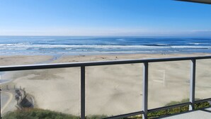 A view of a beach from a balcony with a railing, sandy beach, ocean, and clear sky. - Nye Beach Ocean Front Condo! Walk to Everything! Spectacular Views! (Newport)
