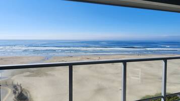 A view of a beach from a balcony with a railing, sandy beach, ocean, and clear sky.