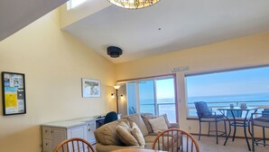 A room with a dining table, chairs, a sofa, a desk, and a large window offering a view of the ocean. - Nye Beach Ocean Front Condo! Walk to Everything! Spectacular Views! (Newport)