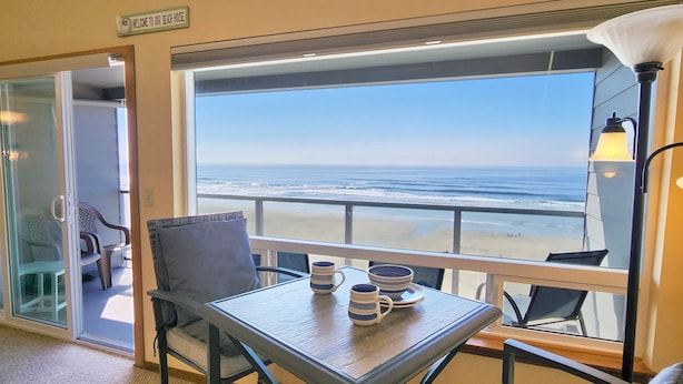 A room with a table and chairs, a view of the beach, and a sign reading "Welcome to our Beach House". - Nye Beach Ocean Front Condo! Walk to Everything! Spectacular Views! (Newport)