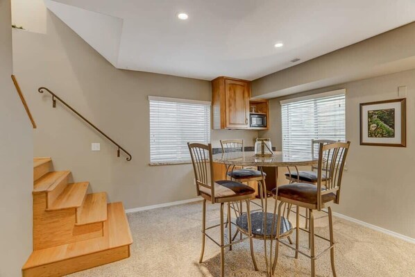 A dining area with a table and chairs, a microwave above the table, and a staircase on the left.