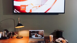 A modern hotel room with a wooden desk, a laptop, a coffee cup, and a television displaying a news channel. - Edenmore Golf and Country Club (Craigavon)