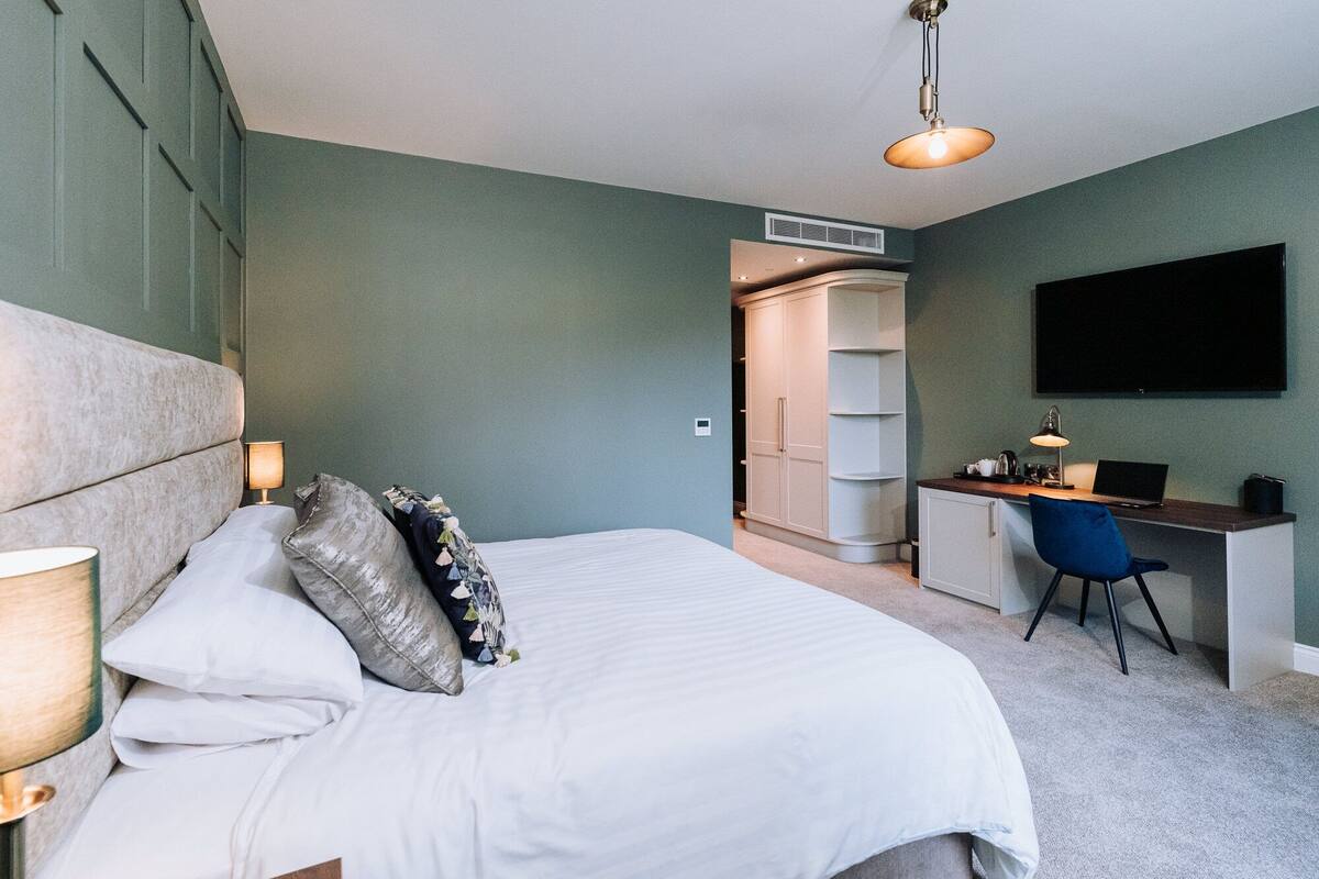 A bedroom with a bed, bedside lamps, a desk with a chair, a TV, and a wardrobe.