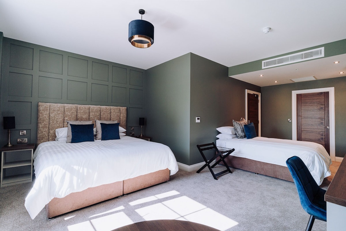 A modern hotel room with two beds, a desk, and a chair.