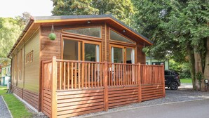 A wooden cabin with a balcony, large windows, and a car parked nearby. - Garuda (Windermere)
