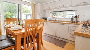 A modern kitchen with white cabinets, a wooden dining table, and a large window overlooking greenery. - Garuda (Windermere)