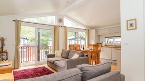 A spacious living area with a grey sofa, wooden dining table, and a red rug. - Garuda (Windermere)