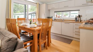 A modern kitchen with white cabinets, a wooden dining table, and chairs. There is a window with curtains, a sink, and various kitchen utensils. - Garuda (Windermere)