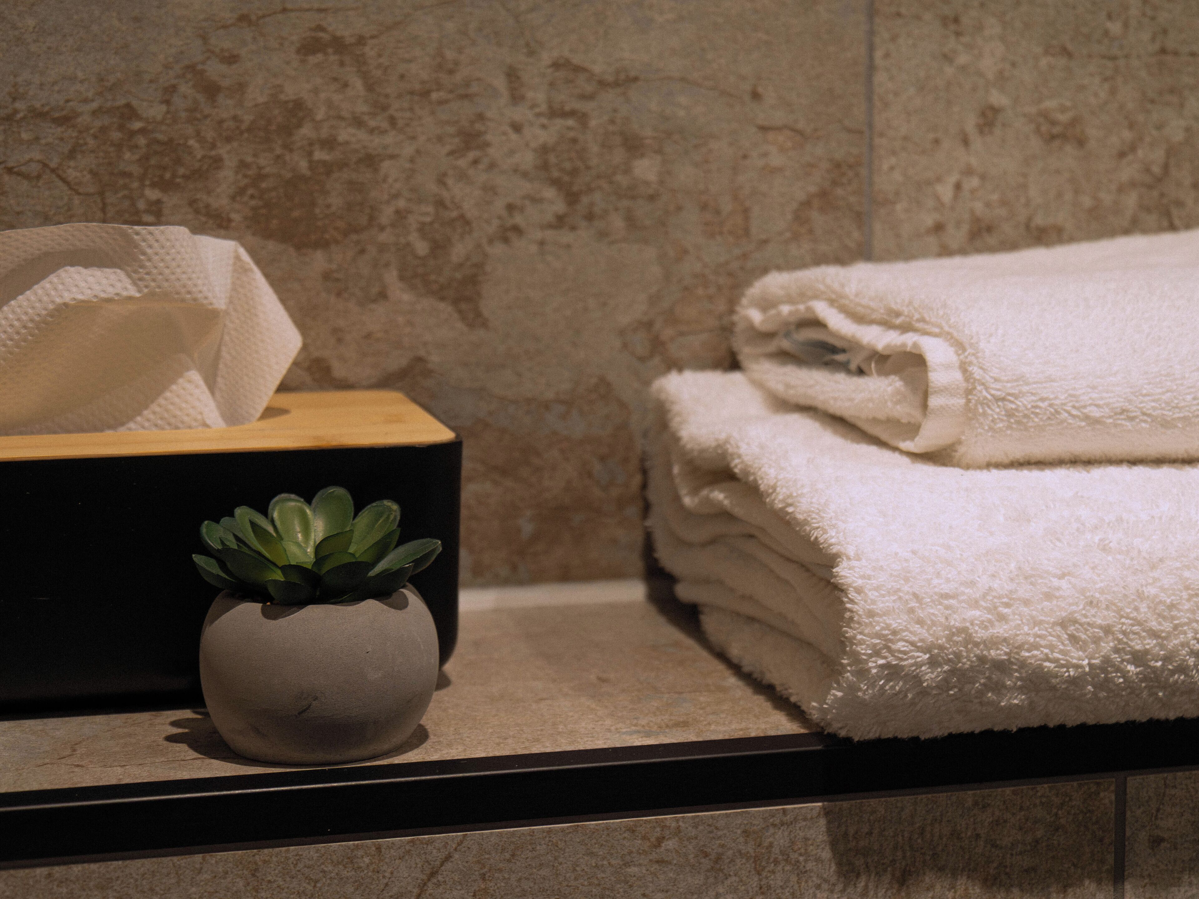 A bathroom with a marble wall, a tissue box, a small potted plant, and neatly folded towels.