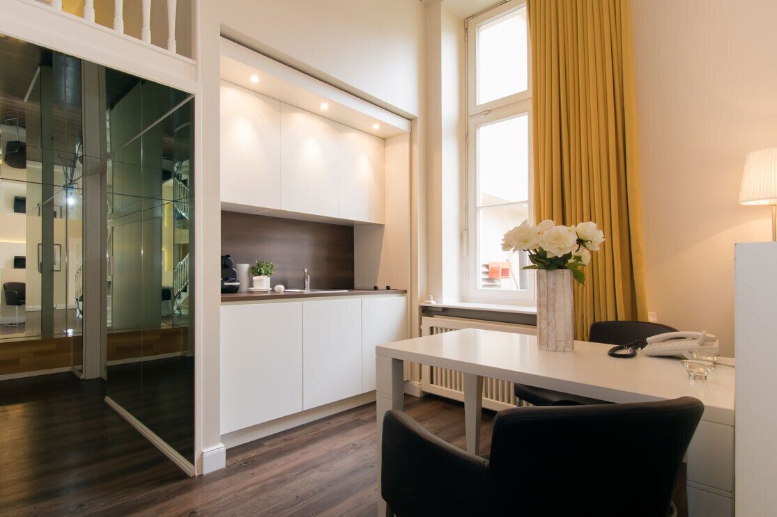 A modern kitchen with white cabinets, a dark countertop, and a window with yellow curtains.