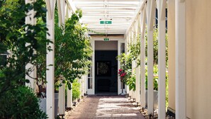 A covered walkway with brick flooring, flanked by white columns and greenery. - Living am Carlsplatz (Düsseldorf)