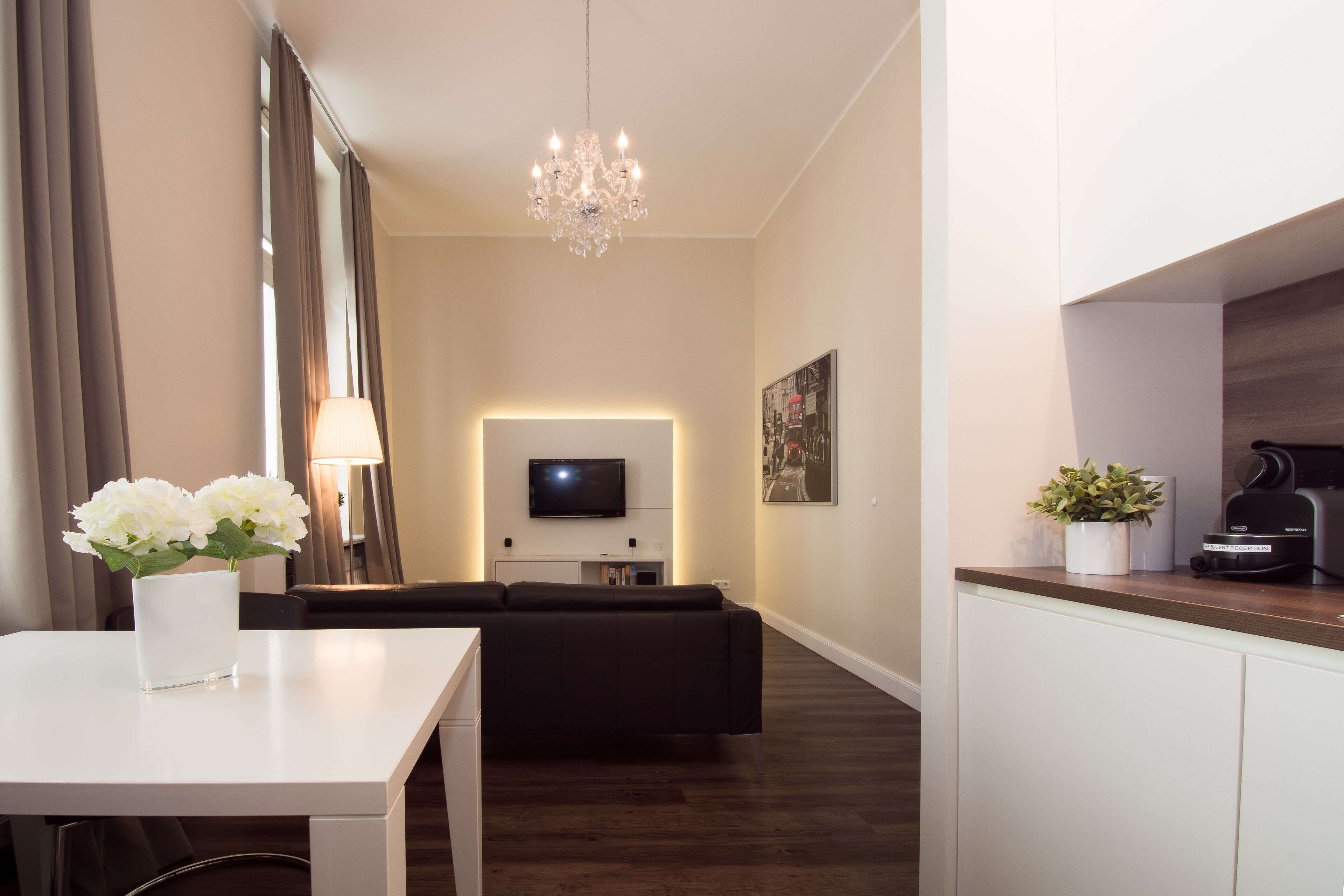 Un salón moderno con un sofá blanco, una mesa de comedor con un florero, una araña y un televisor de pantalla plana montado en la pared.