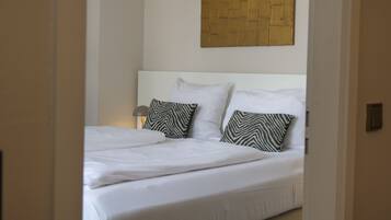 A neatly made bed with white linens and two patterned pillows, a bedside lamp, and a wooden panel on the wall above the bed.