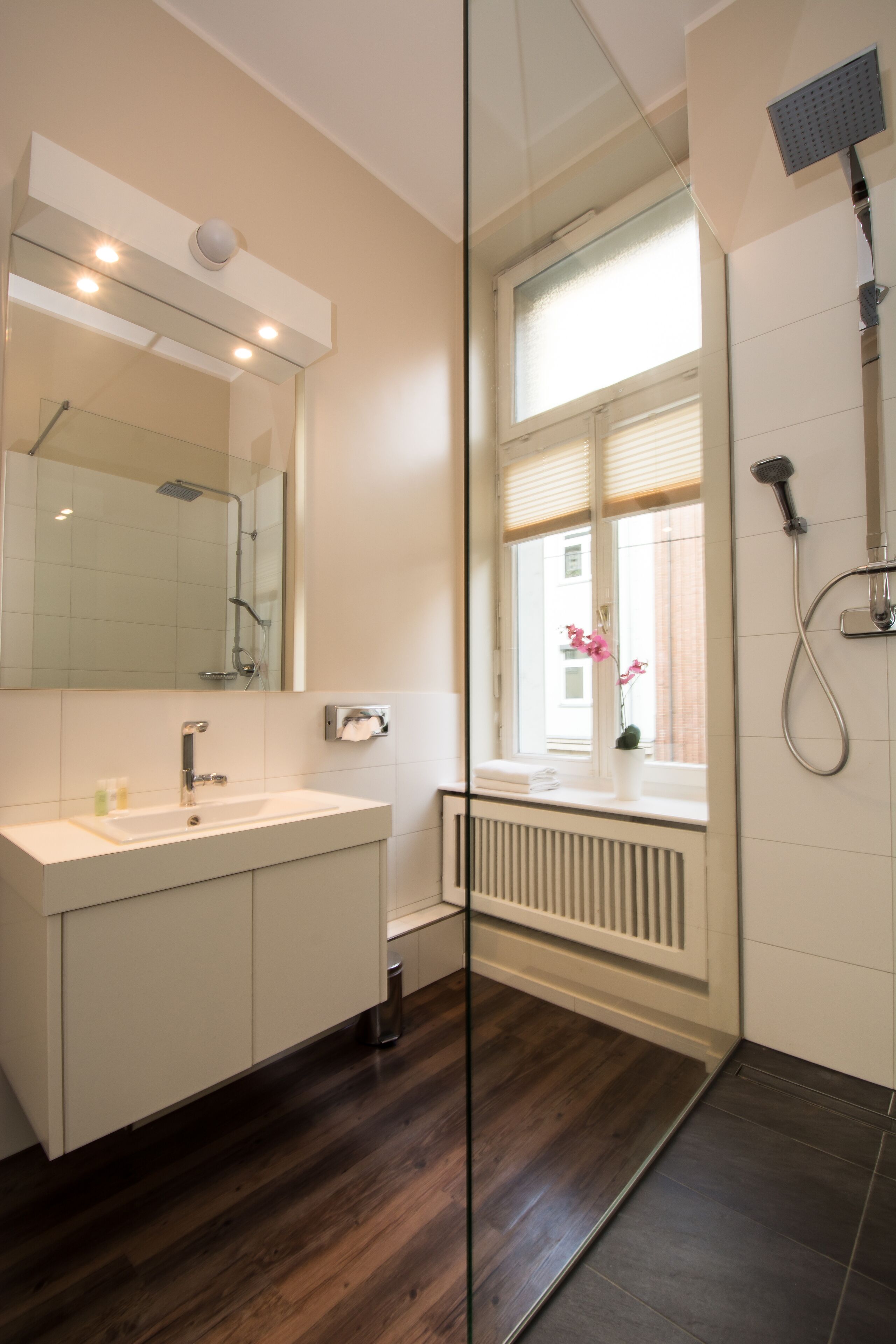 A modern bathroom with a large mirror, a shower, and a window with a view of the outside.