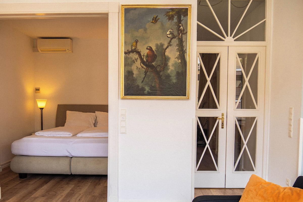 Ein Hotelzimmer mit einem Bett, einem Vogelgemälde an der Wand und einer Tür mit Glasfeldern.