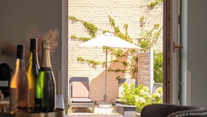 A patio area with a table, chairs, and a white umbrella. There are bottles on the table, and a brick wall in the background. - Living am Carlsplatz (Düsseldorf)