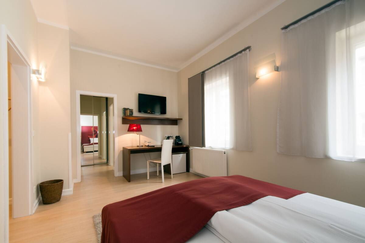 Ein Hotelzimmer mit Bett, Schreibtisch, Stuhl, Fernseher und einem fenster mit Vorhängen.