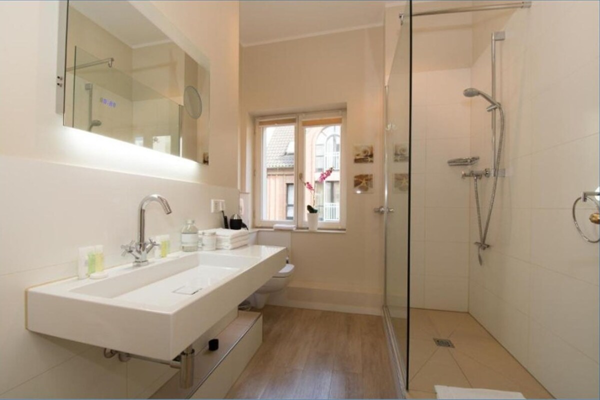 A modern bathroom with a large sink, a glass shower enclosure, and a window providing natural light.