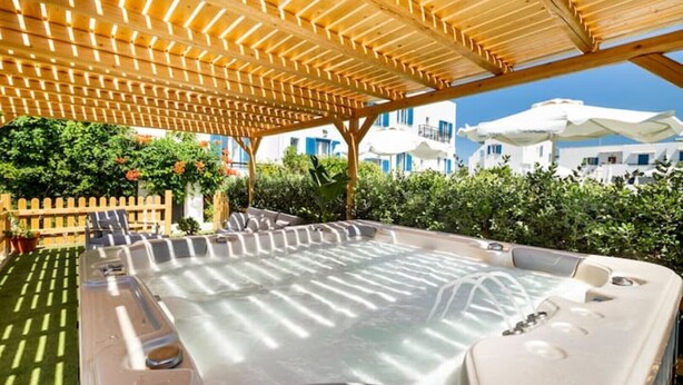 A hot tub area with a wooden pergola overhead, surrounded by greenery and white buildings in the background. - Ikaros Studios - Pool & Jacuzzi, 5 mins from beach (Naxos)