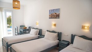 A hotel room with two single beds, a small table with chairs, and a balcony with a view of a coastal town. - Ikaros Studios - Pool & Jacuzzi, 5 mins from beach (Naxos)