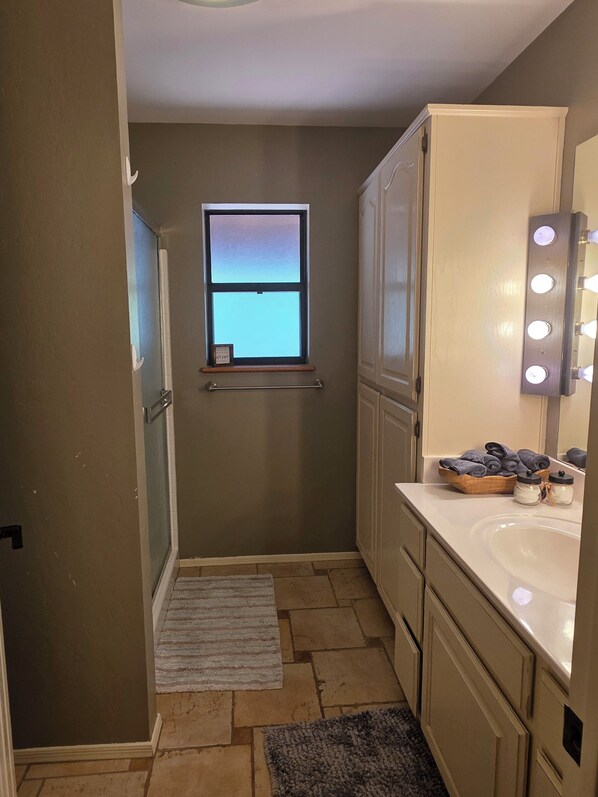A bathroom with a vanity, a mirror with lights, a window, and a towel rack.