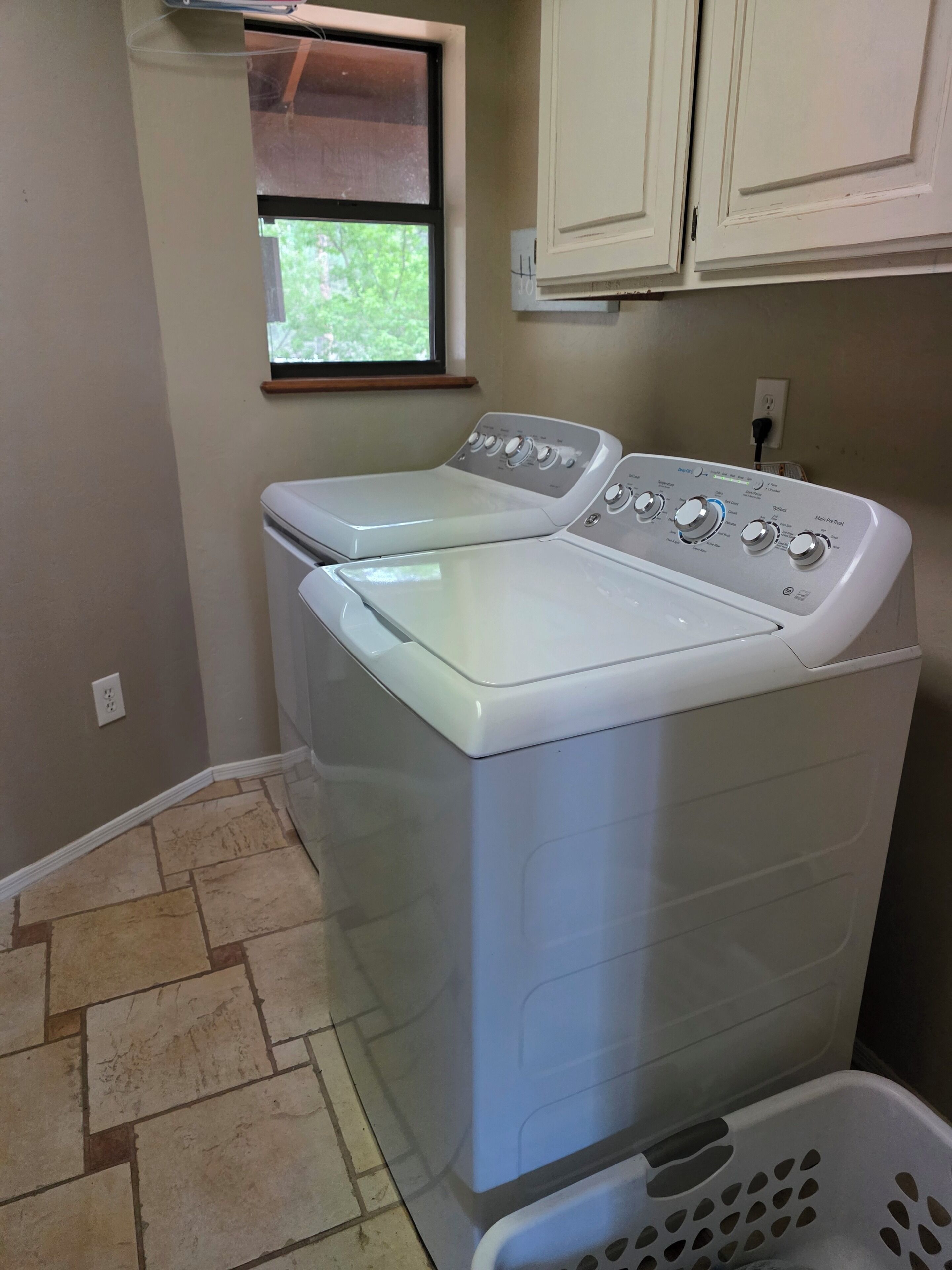 A laundry room with two front-loading washing machines, a window, and a laundry basket.