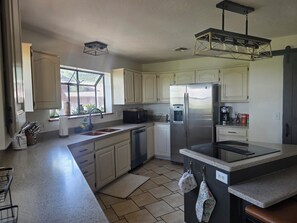 A kitchen with white cabinets, a stainless steel refrigerator, a coffee maker, and a window with a view of greenery.