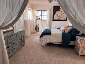 Une chambre à coucher avec un lit, une commode, un fauteuil suspendu et un tableau accroché au mur.