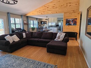 A modern living room with a sectional sofa, a patterned rug, and a view into the kitchen.