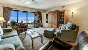 A spacious living room with a large window, a ceiling fan, and a view of the sea. - 303 Atlantis 2 Bedroom Condo by RedAwning (Fernandina Beach)