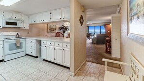 A kitchen with white cabinets, a microwave, and a stove. There is a dining area with a table and chairs, and a view of the outside. - 303 Atlantis 2 Bedroom Condo by RedAwning (Fernandina Beach)