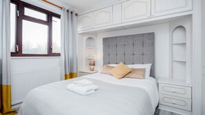 Quarto de hotel com uma cama grande, mesa de cabeceira com abajur, janela com cortinas e um guarda-roupa embutido.
