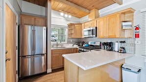 A modern kitchen with wooden cabinets, stainless steel appliances, and a white countertop. - Heart of Capitola Vacation Rental (Capitola)