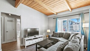 A modern living room with a sectional sofa, a flat-screen TV, a coffee table, and a wooden ceiling. - Heart of Capitola Vacation Rental (Capitola)