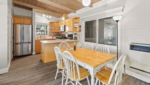 A modern kitchen with wooden cabinets, a stainless steel refrigerator, and a dining area with a wooden table and white chairs. - Heart of Capitola Vacation Rental (Capitola)