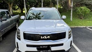 A white Kia vehicle parked in a lot with palm trees and a clear sky in the background. - Turtle Bay Golf Course View. Updated 1-bed w/*AC, covered lanai, end unit (Kahuku)