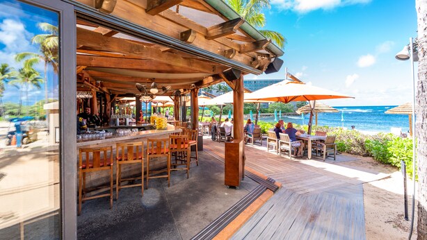 An outdoor bar area with wooden furniture and a view of the ocean. - Turtle Bay Golf Course View. Updated 1-bed w/*AC, covered lanai, end unit (Kahuku)