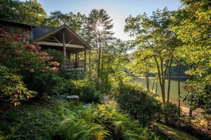 A wooden gazebo with a balcony overlooking a lake, surrounded by lush greenery and trees. - Lake front with private dock, fire pit, hammock, pool table & gorgeous views! Fishing poles, paddle boards & canoe provided. (Cullowhee)